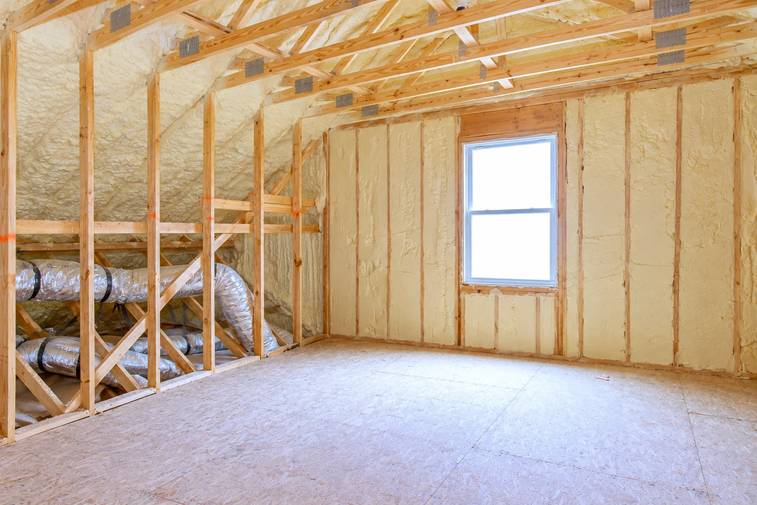 Unfinished room with yellow spray foam insulation between wooden wall studs and roof trusses, plus a window and exposed ductwork.